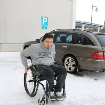 Mies pyörätuolissa auto parkkeerattu invapaikalle.