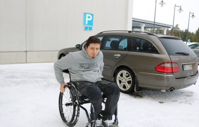 Mies pyörätuolissa auto parkkeerattu invapaikalle.